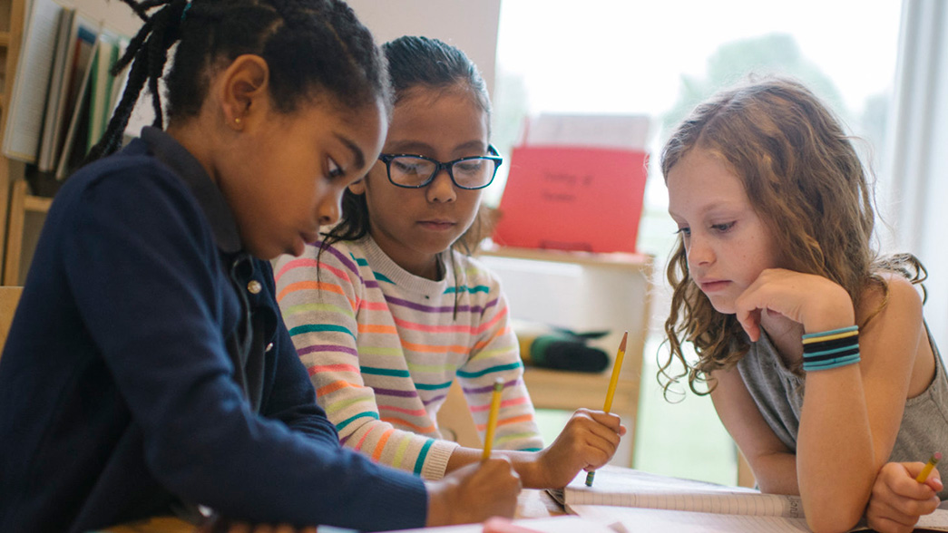 Three girls sitting at a table in an elementary classroom working on a project. 